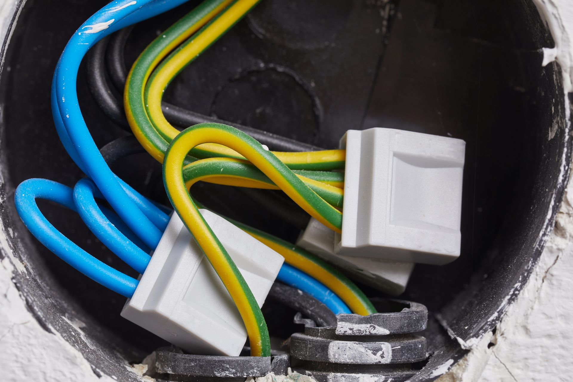 Electrical junction box with blue, green, and yellow wires and two white connectors inside a wall opening