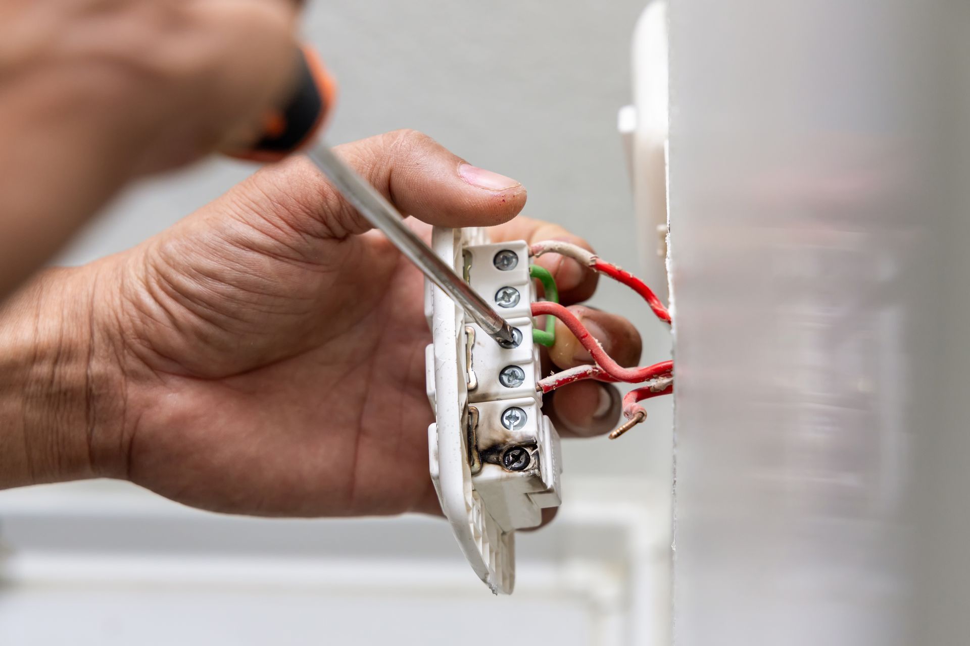 Hand wiring a wall switch with a screwdriver, red and white wires visible
