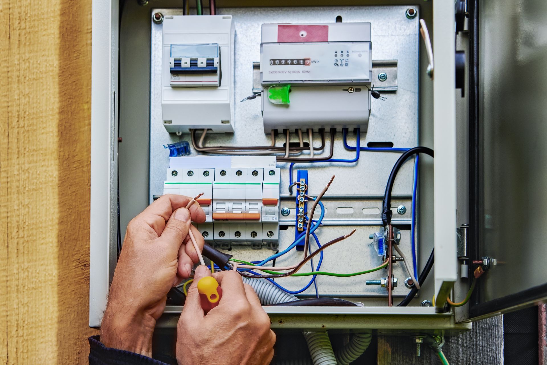 Technician wiring an open electrical breaker panel with tools inside a cabinet