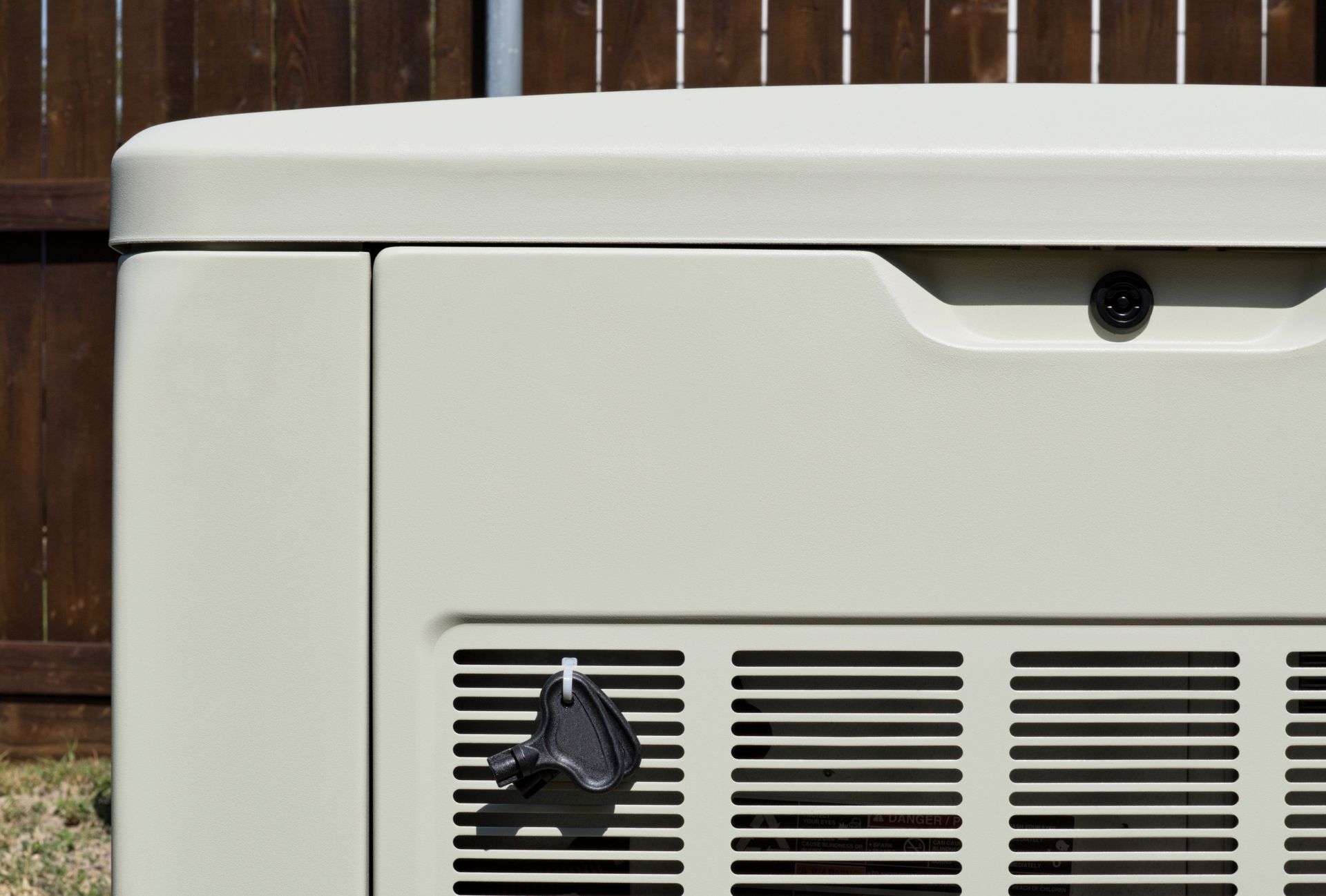 White outdoor HVAC unit against a wooden fence, with vents and a black hose connection.