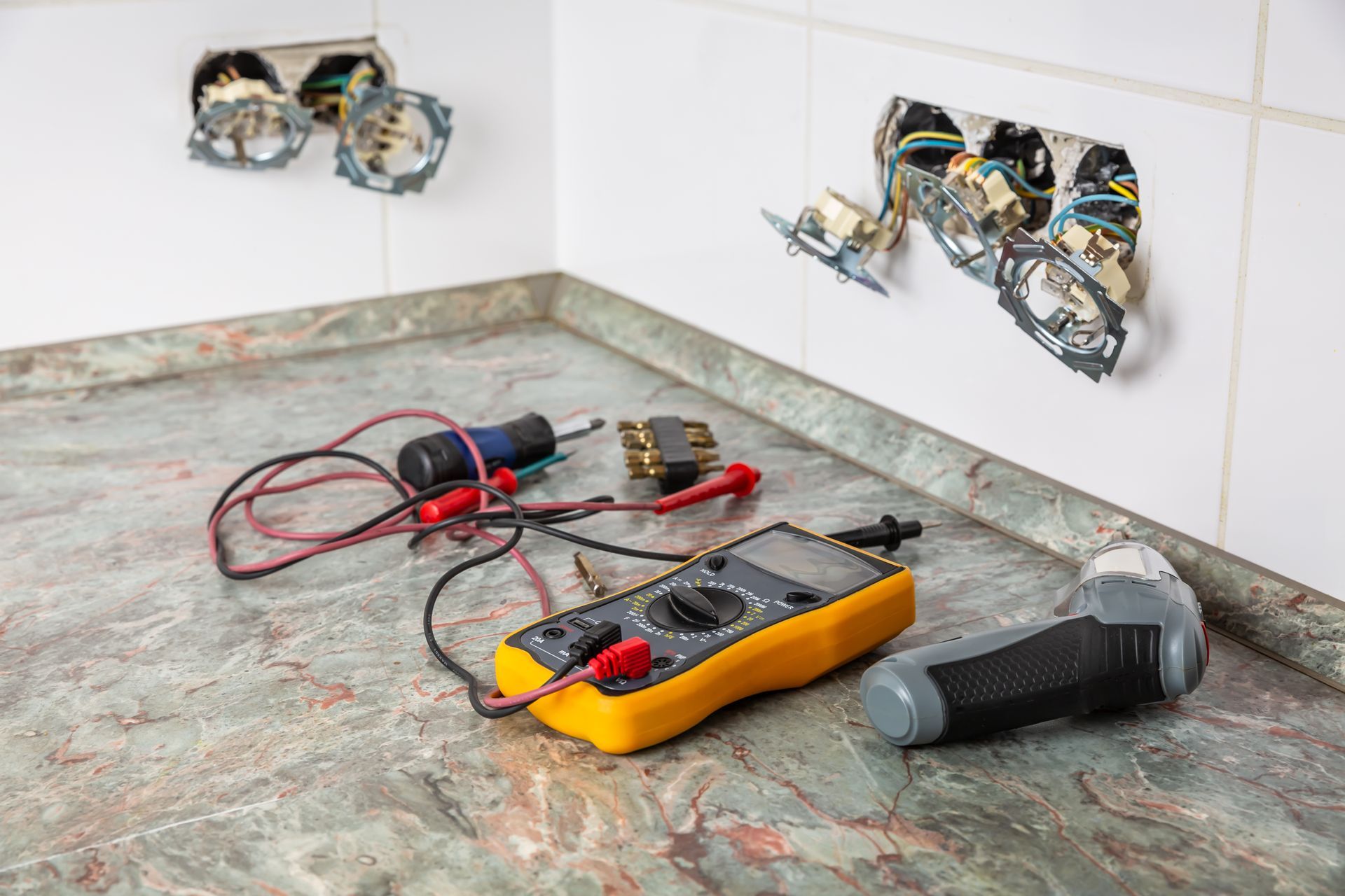 Tools on a countertop beside open electrical wall boxes with exposed wires