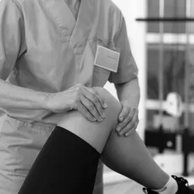 Photo en noir et blanc d'une personne se faisant examiner le genou par un médecin
