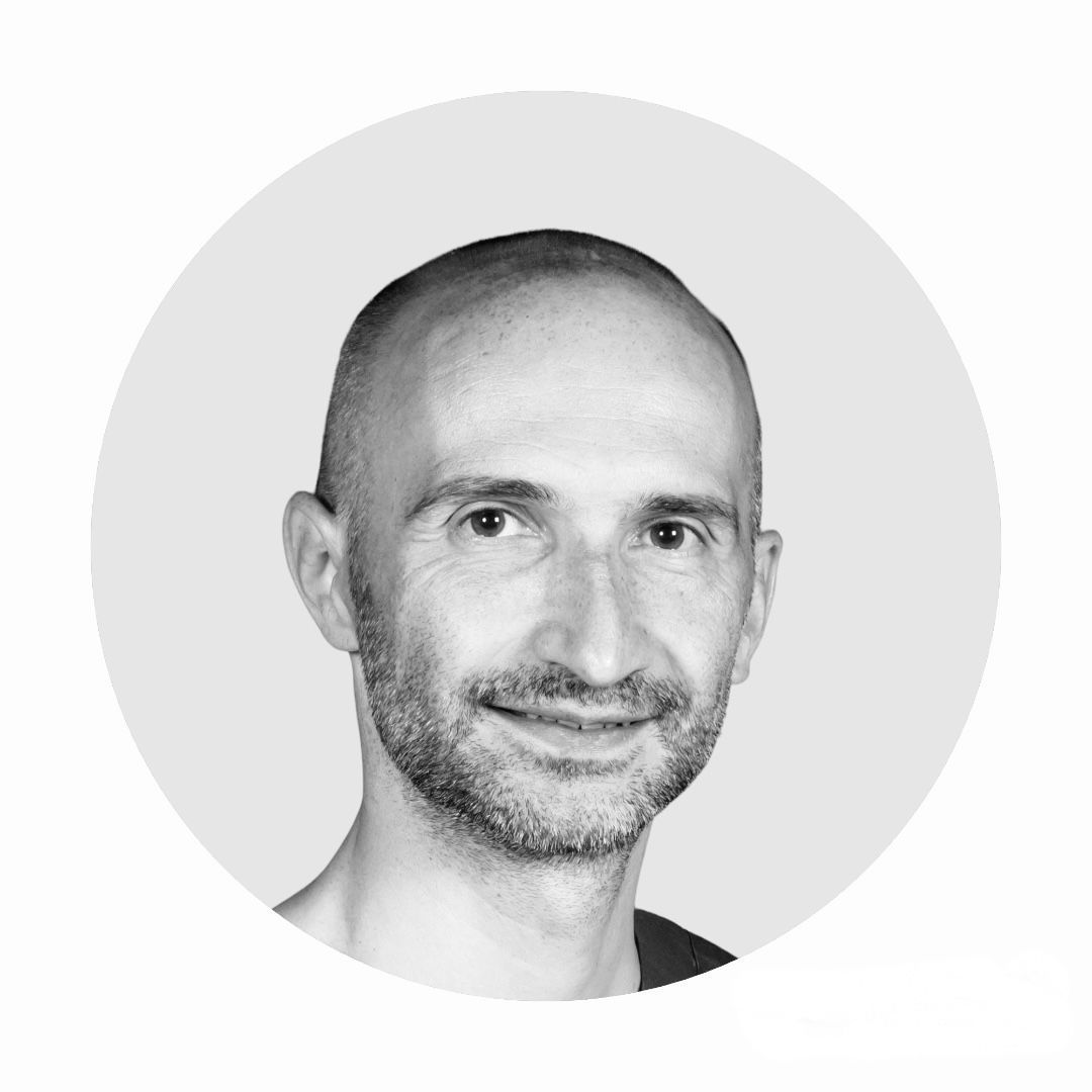 Un homme barbu sourit sur une photo en noir et blanc.