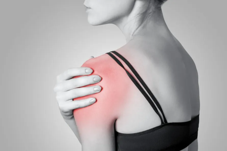 Une femme se tient l’épaule de douleur.