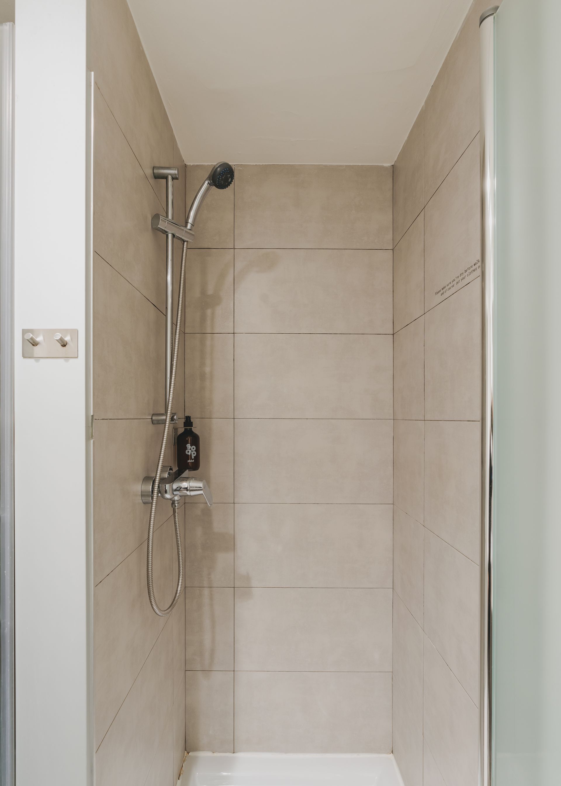 A shower with a shower head and a soap dispenser on the wall.
