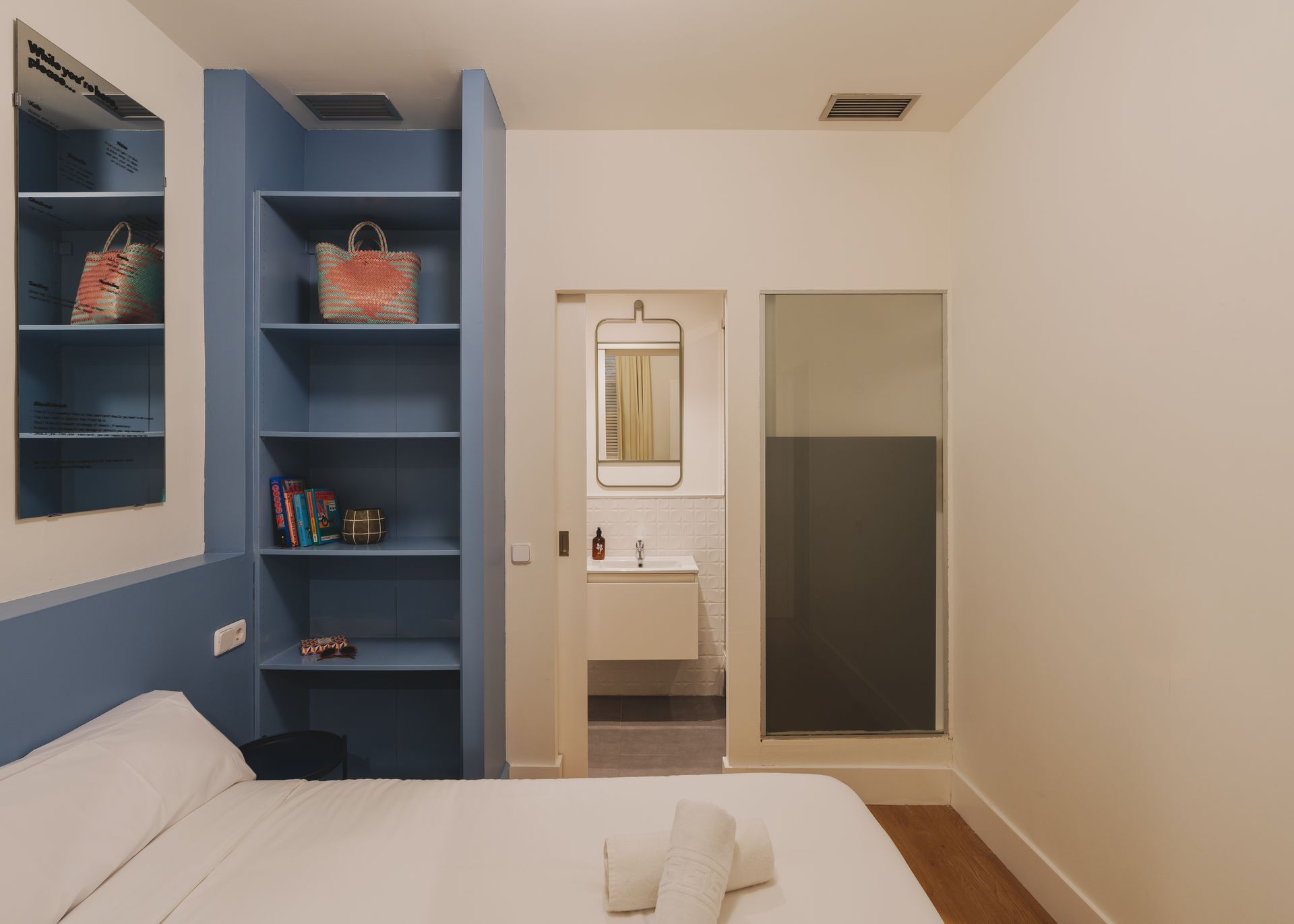 A bedroom with a bed , shelves , a mirror and a bathroom.