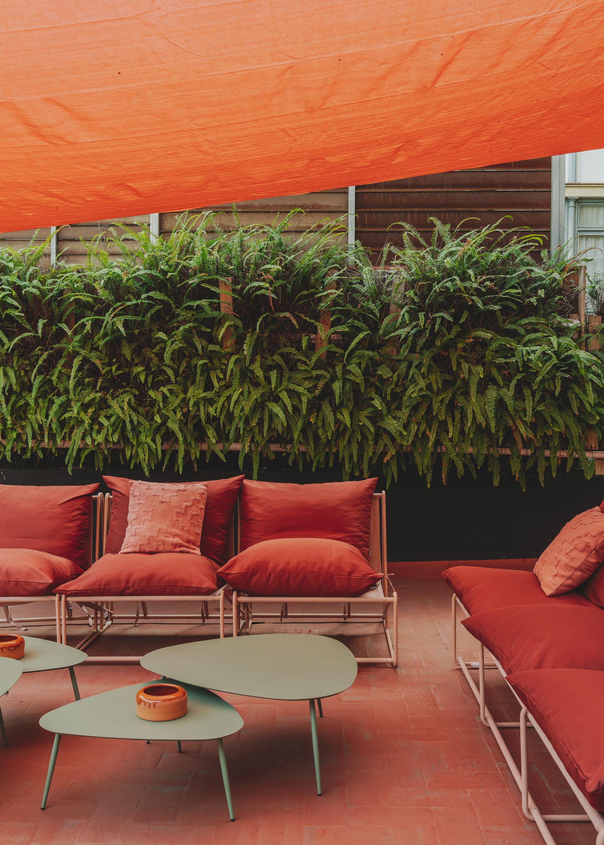 A patio with a couch , chairs and tables under an orange umbrella.