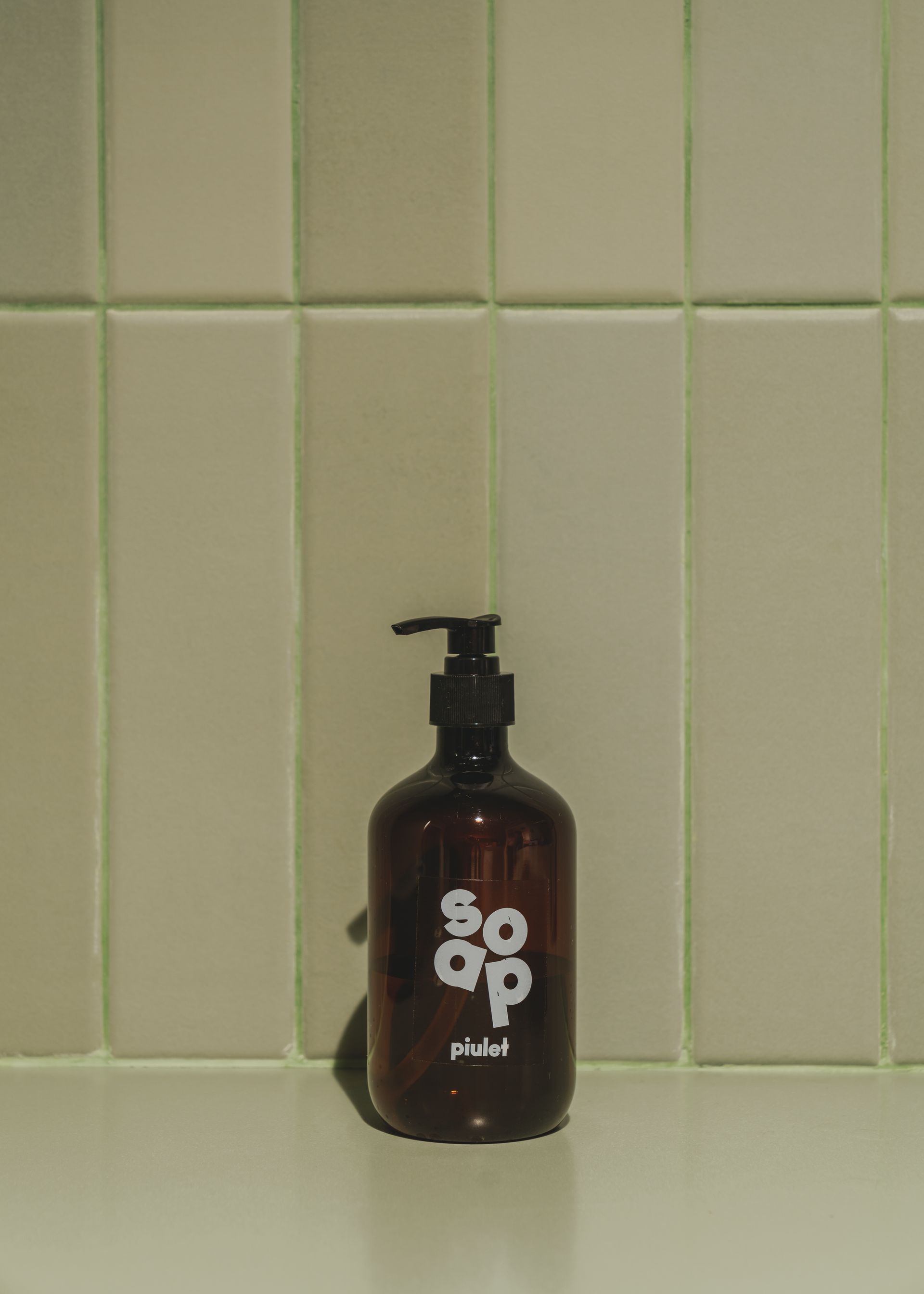 A bottle of soap is sitting on a counter in front of a tiled wall.