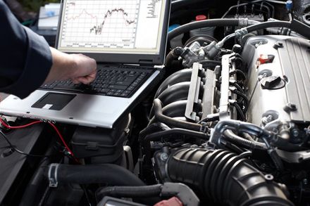 Mechanic using a laptop to diagnose a car engine, displaying graphs.
