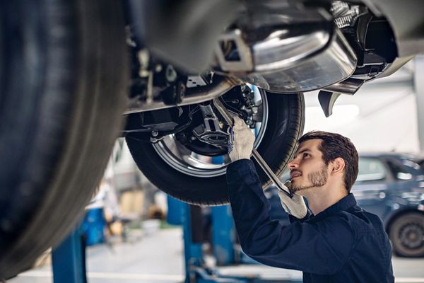 Mechanic in blue uniform working under a car, examining its underside in a garage.