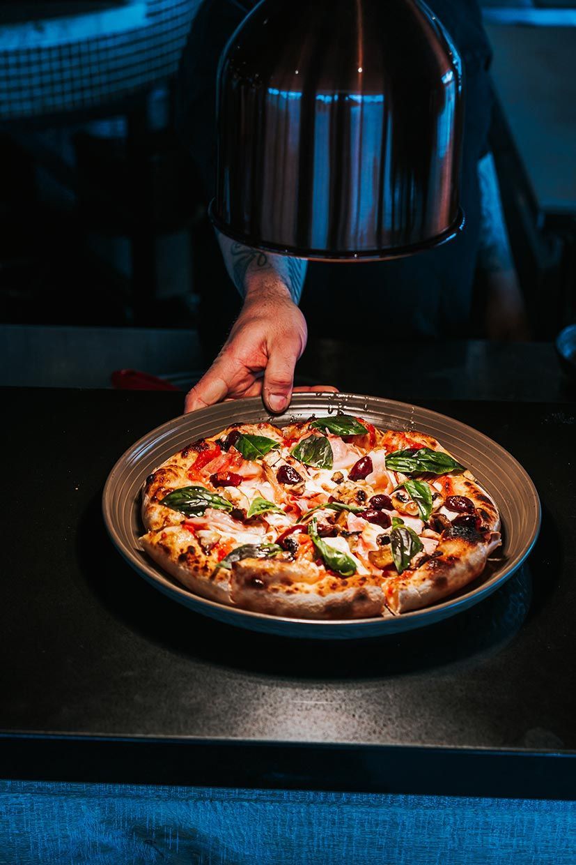 A Person is Holding a Pizza on a Plate on a Table — Fedeles East Gosford in East Gosford, NSW