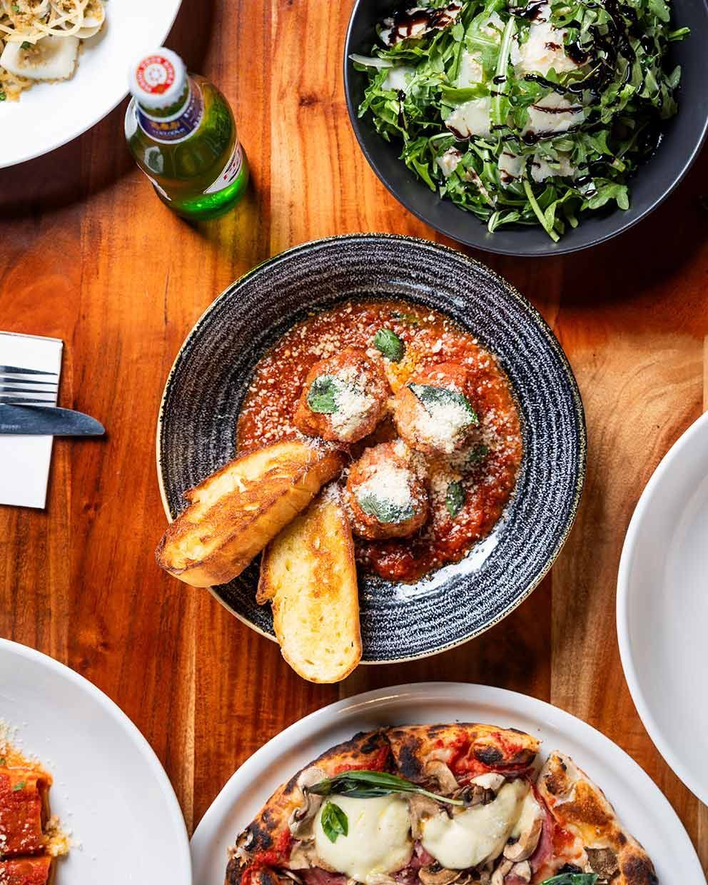 A Wooden Table Topped With Plates of Food and a Bowl of Salad — Fedeles East Gosford in East Gosford, NSW