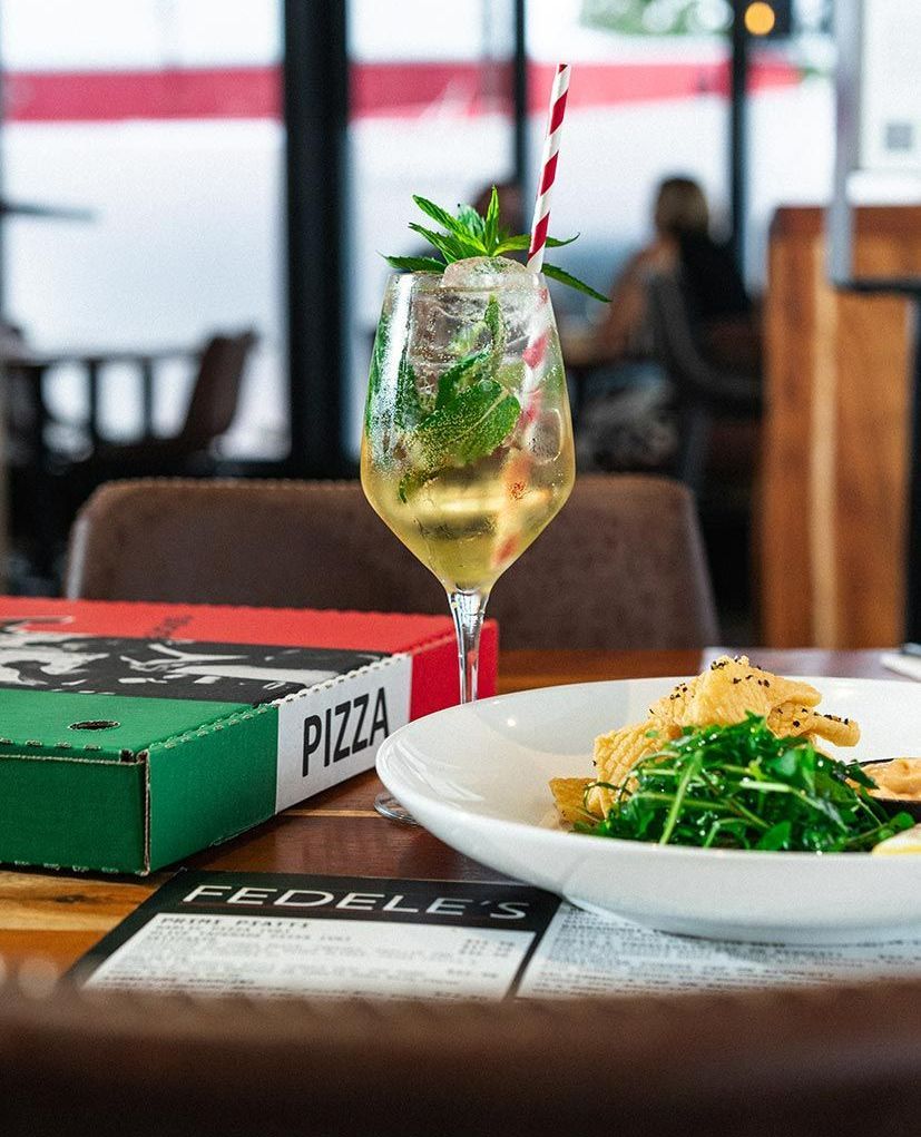 A Pizza Box is Sitting on a Table Next to a Plate of Food and a Glass of Wine — Fedeles East Gosford in East Gosford, NSW