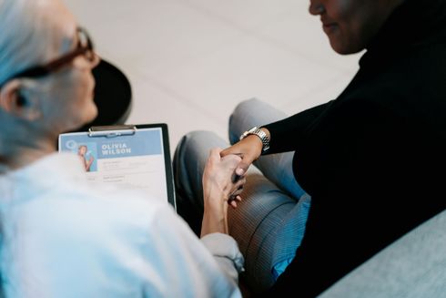 A woman is holding another woman 's hand while sitting on the floor.