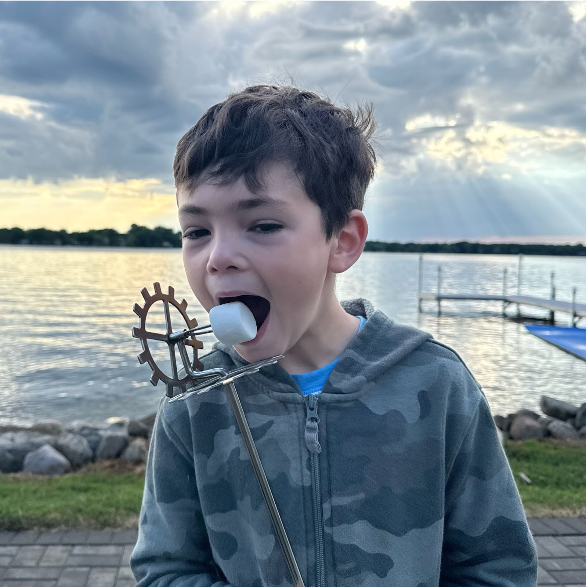A young boy is eating a marshmallow by the water
