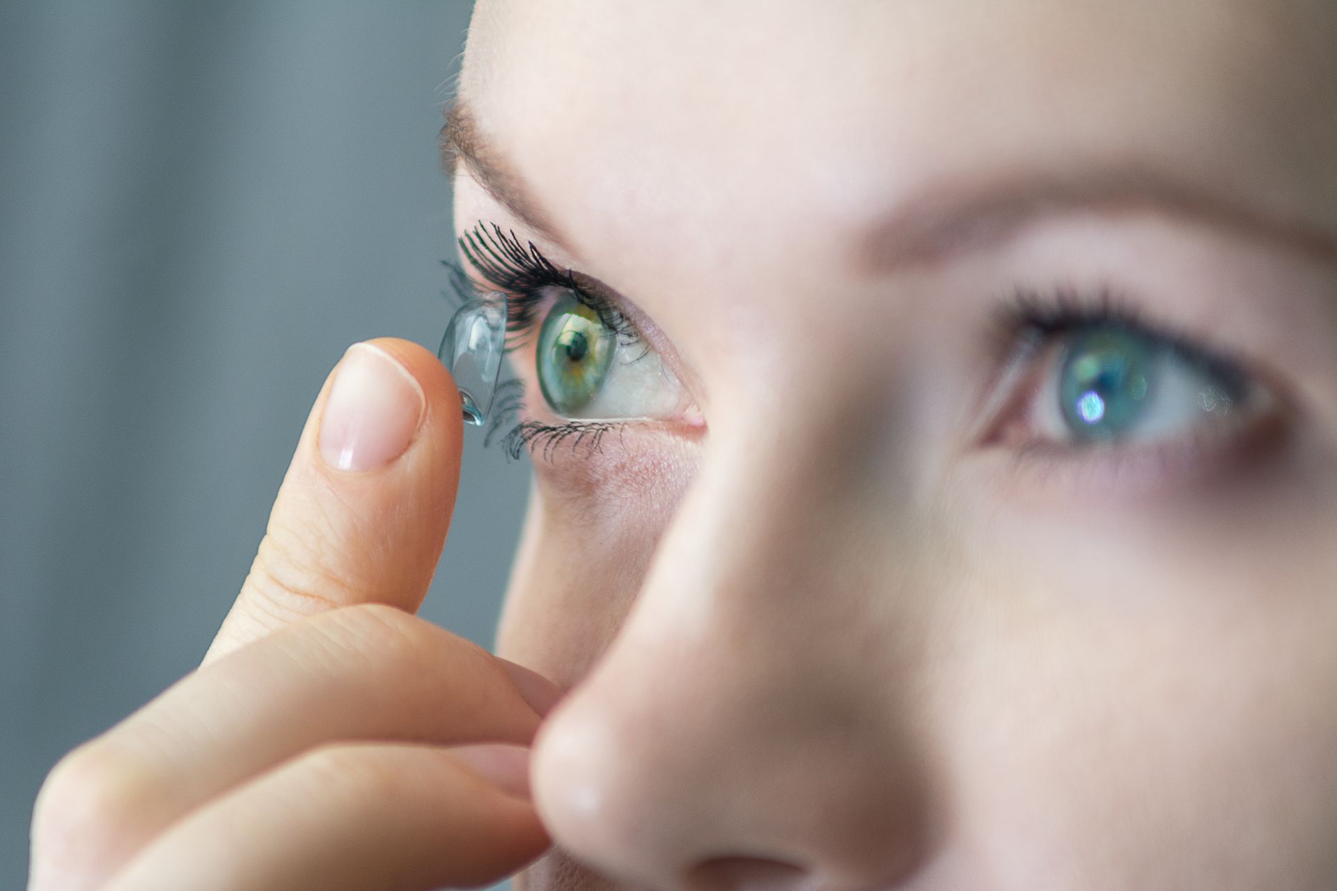 A woman is putting a contact lens in her green eye.