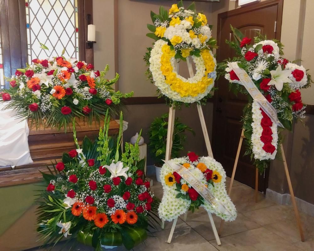 Funeral flower arrangements: wreaths, crosses, and bouquets with red, white, orange, and yellow flowers.