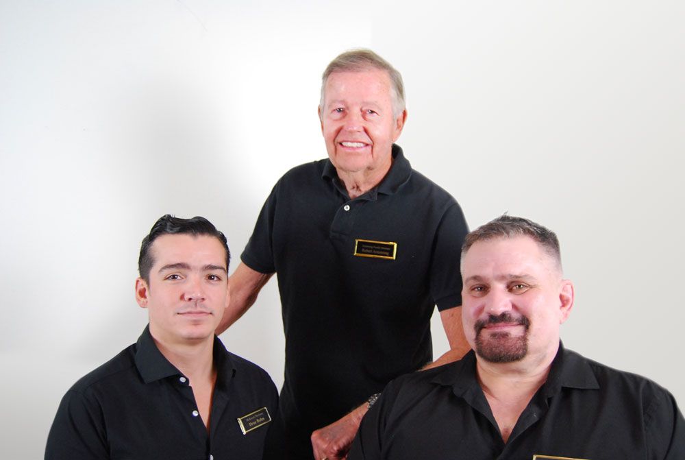 Three men in black shirts smiling in front of a white background.