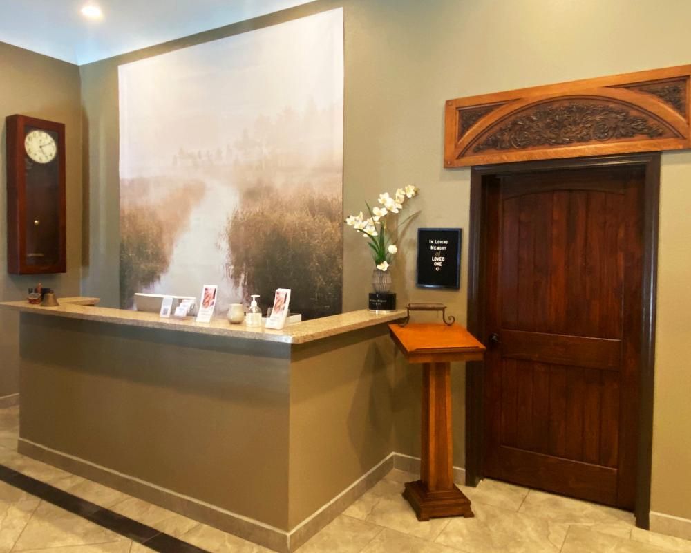 Reception desk in a spa-like setting with a large landscape print, wooden door and clock.