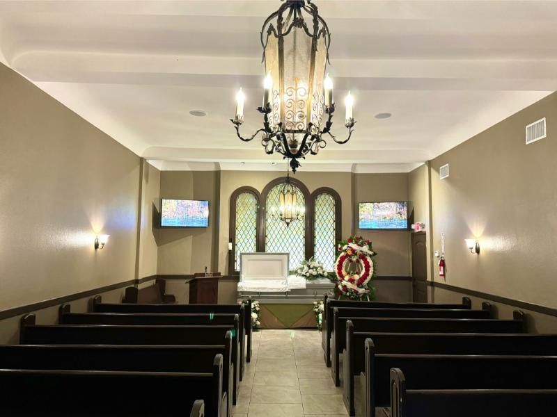 Interior of a funeral chapel with rows of pews, a casket, and a floral arrangement.