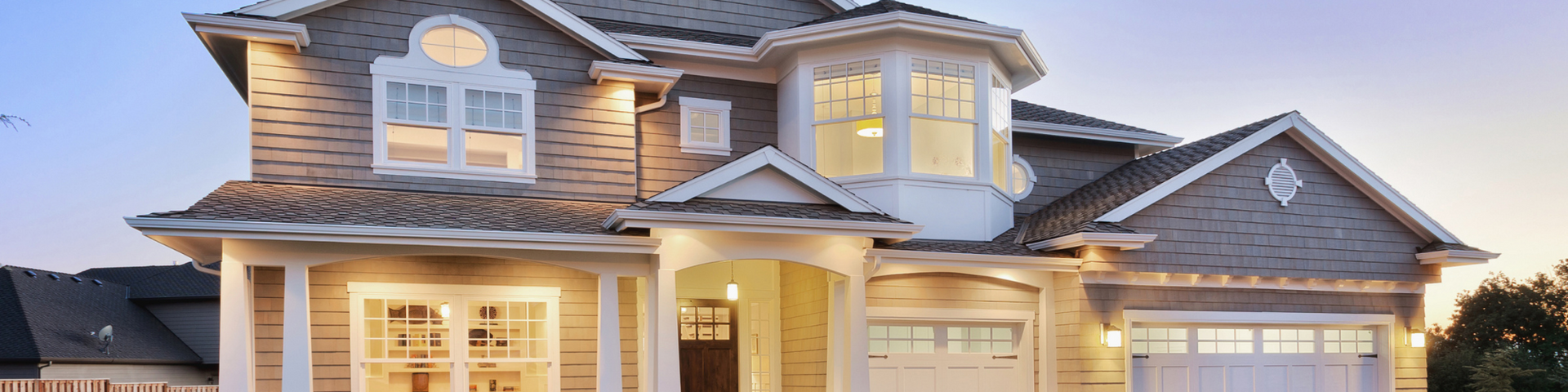 Two-story suburban house with warm exterior lights and a covered front entry at dusk