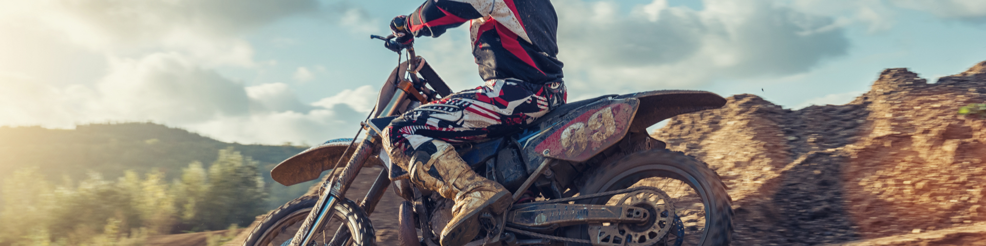Motocross rider in red and black gear riding on a dirt trail with mountains in the background