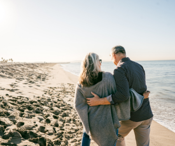Two people walking arm-in-arm along a sandy beach at sunset