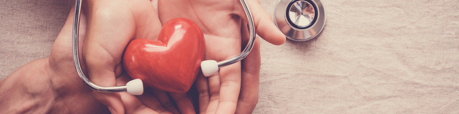 Hands holding a red heart with a stethoscope, symbolizing health care.