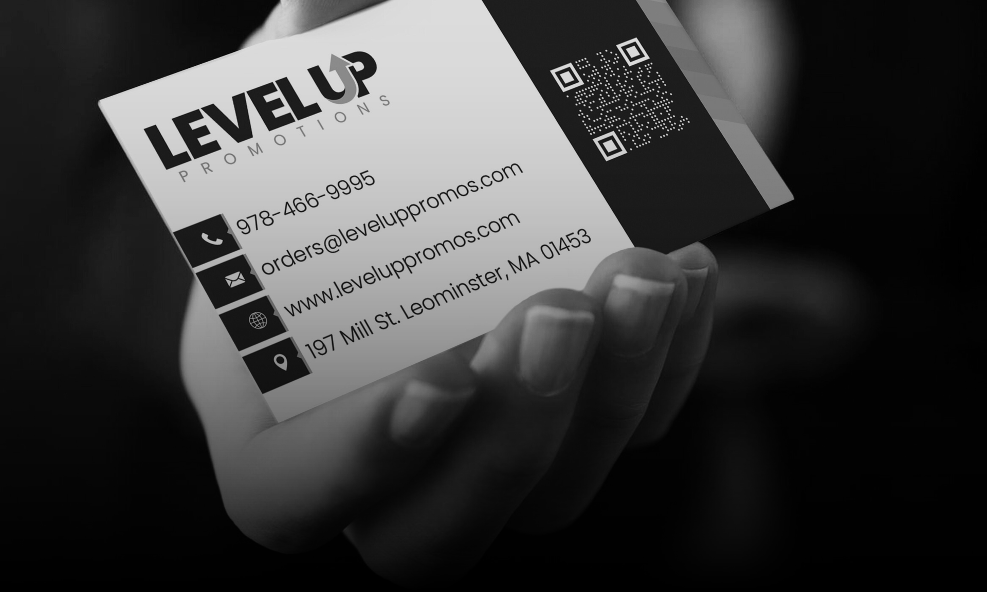 Business card for Level Up Promotions held in hand, black and white.