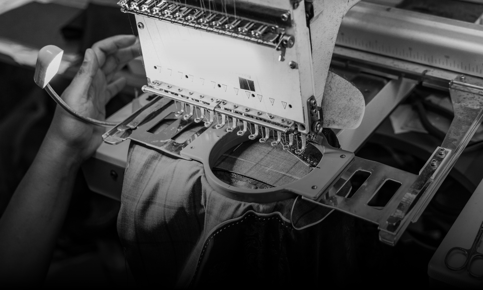 An embroidery machine stitching on a hat, operated by a person's hands.