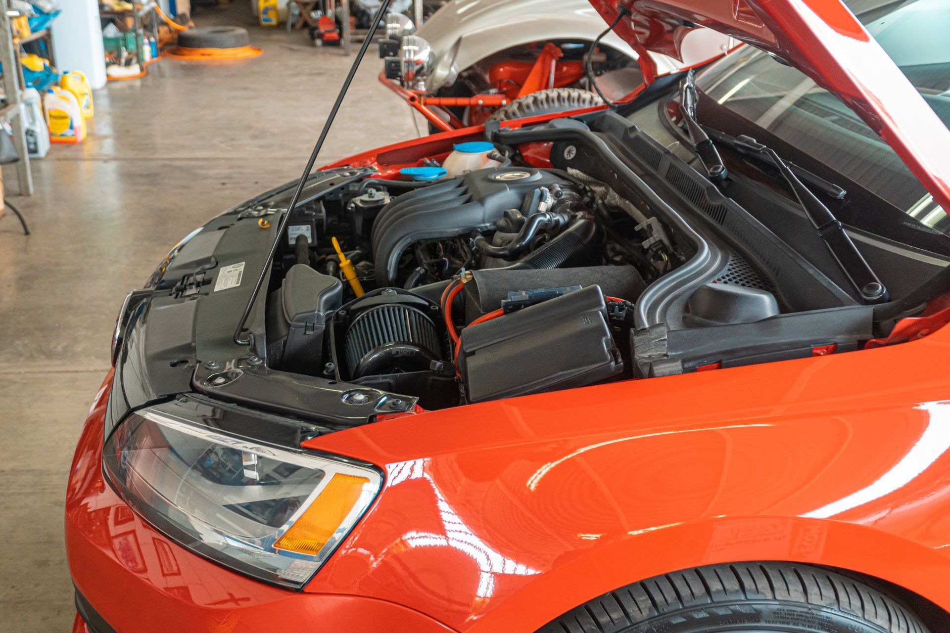 A red car with its hood open in a garage.