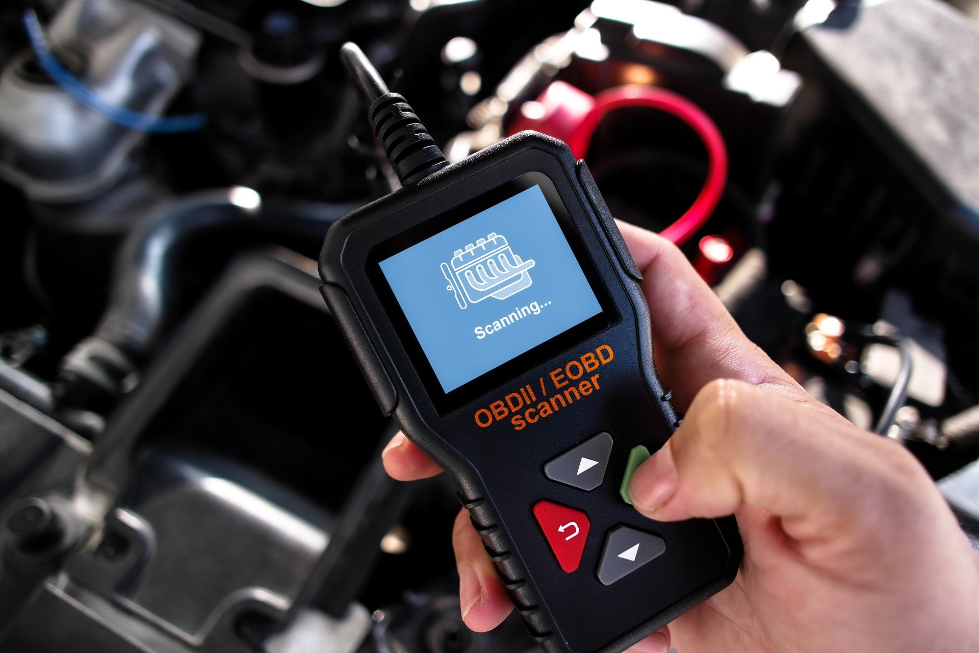 A person is holding a scanner in front of a car engine.