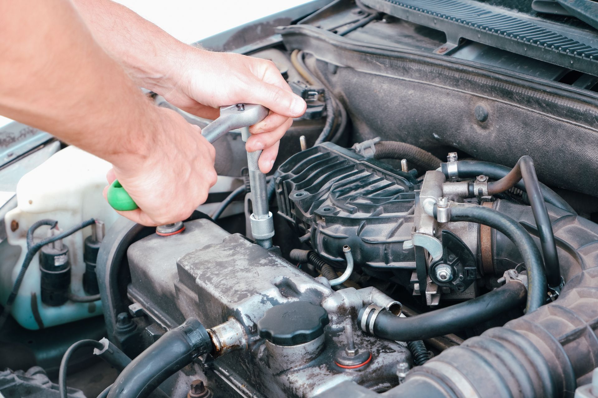 A man is working on the engine of a car with a wrench.