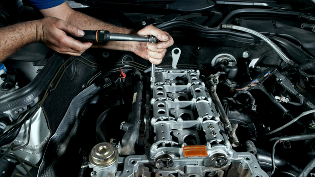 A man is working on a car engine with a wrench.