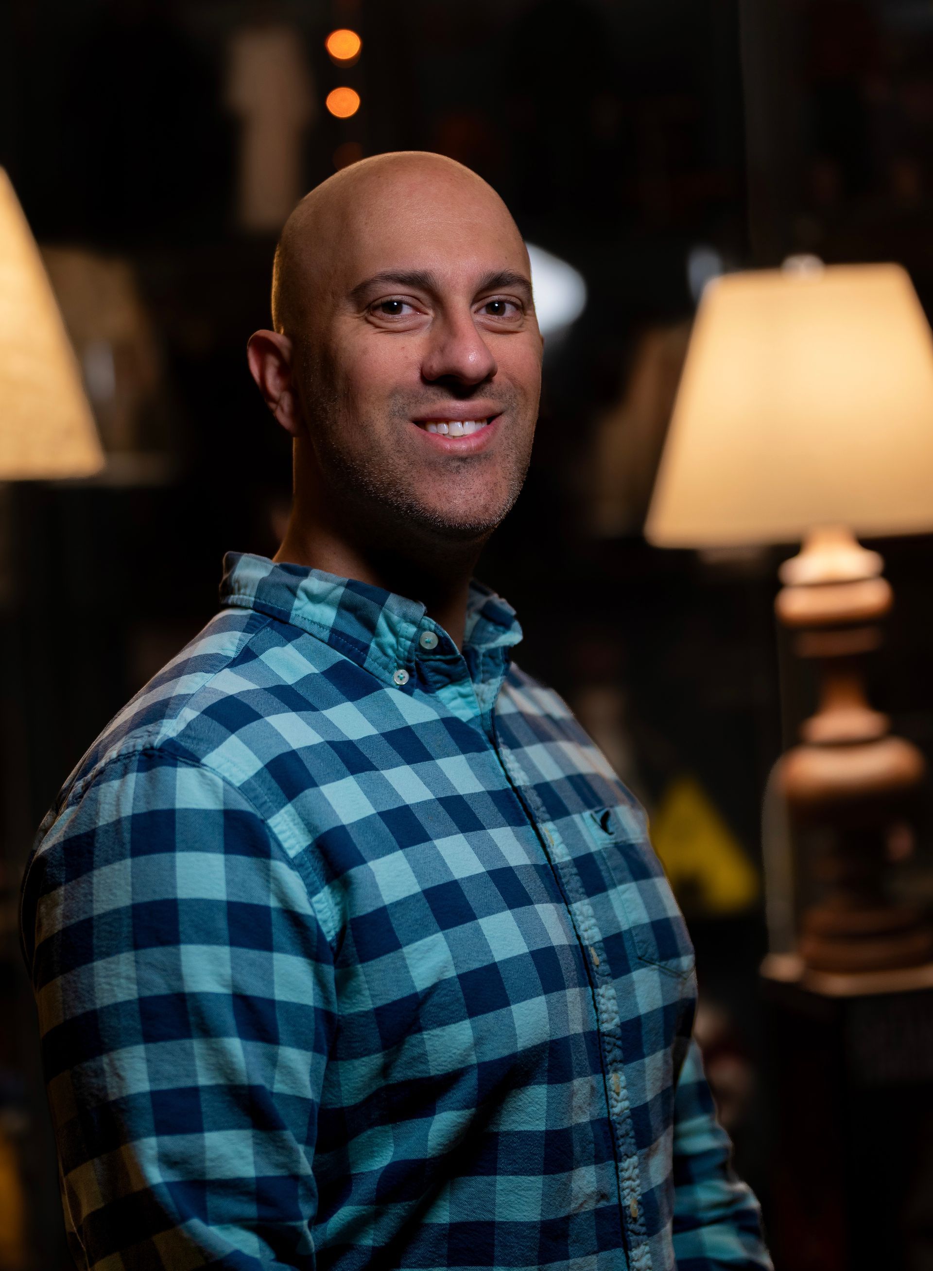 A bald man in a plaid shirt is standing in front of a lamp.