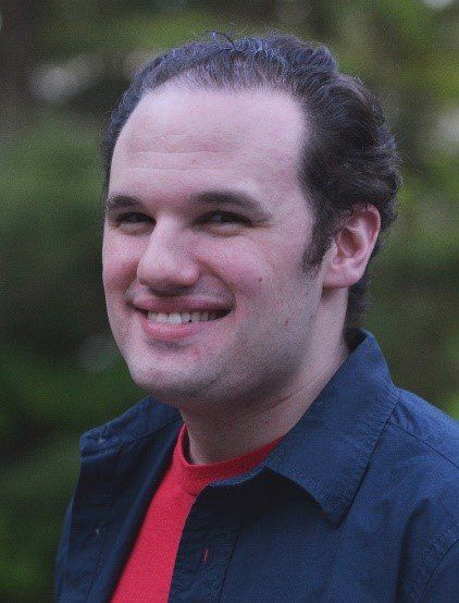 A man wearing a blue jacket and a red shirt is smiling.