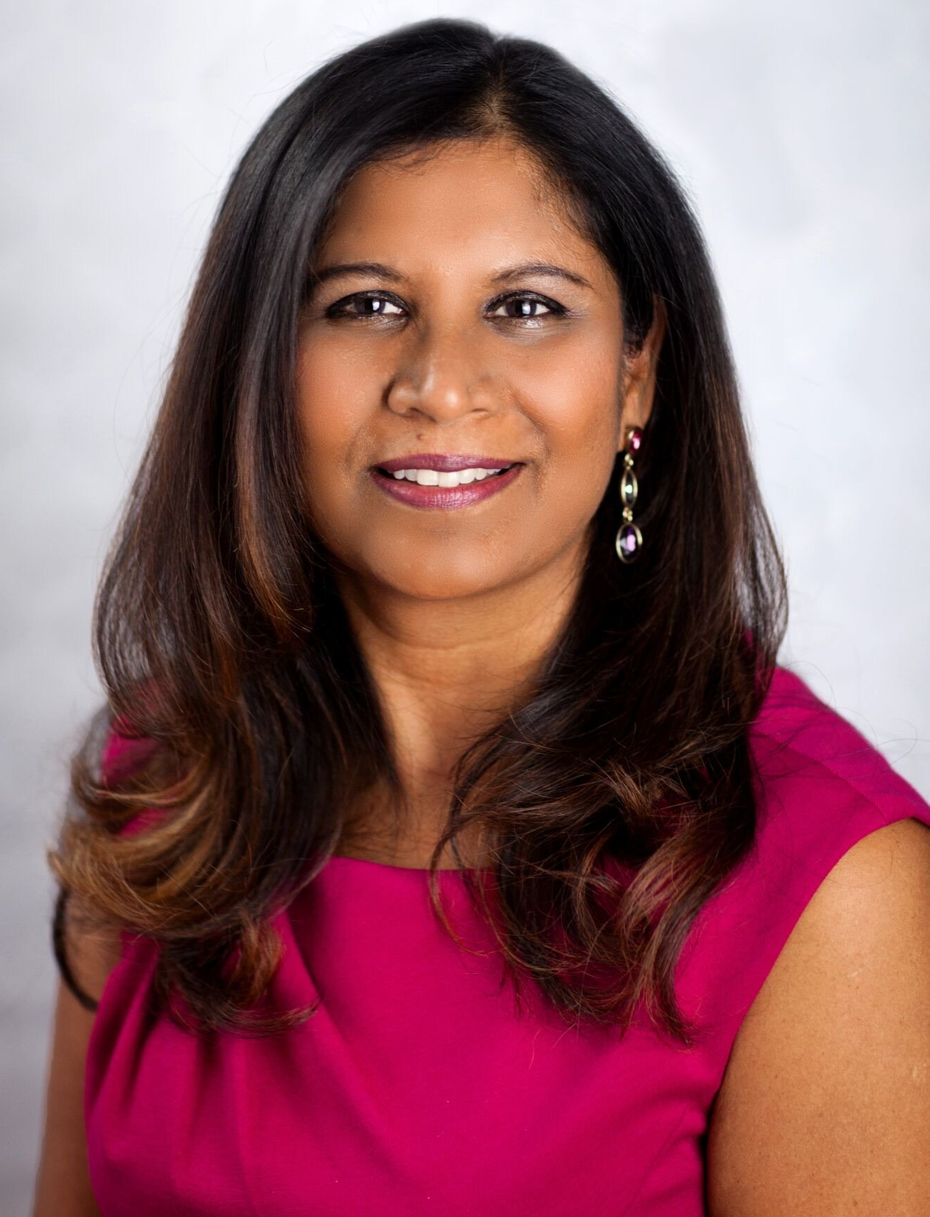 A woman in a pink dress and earrings is smiling for the camera.