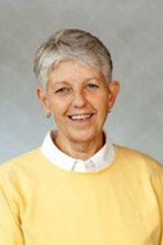 A woman wearing a yellow sweater and a white shirt is smiling for the camera.