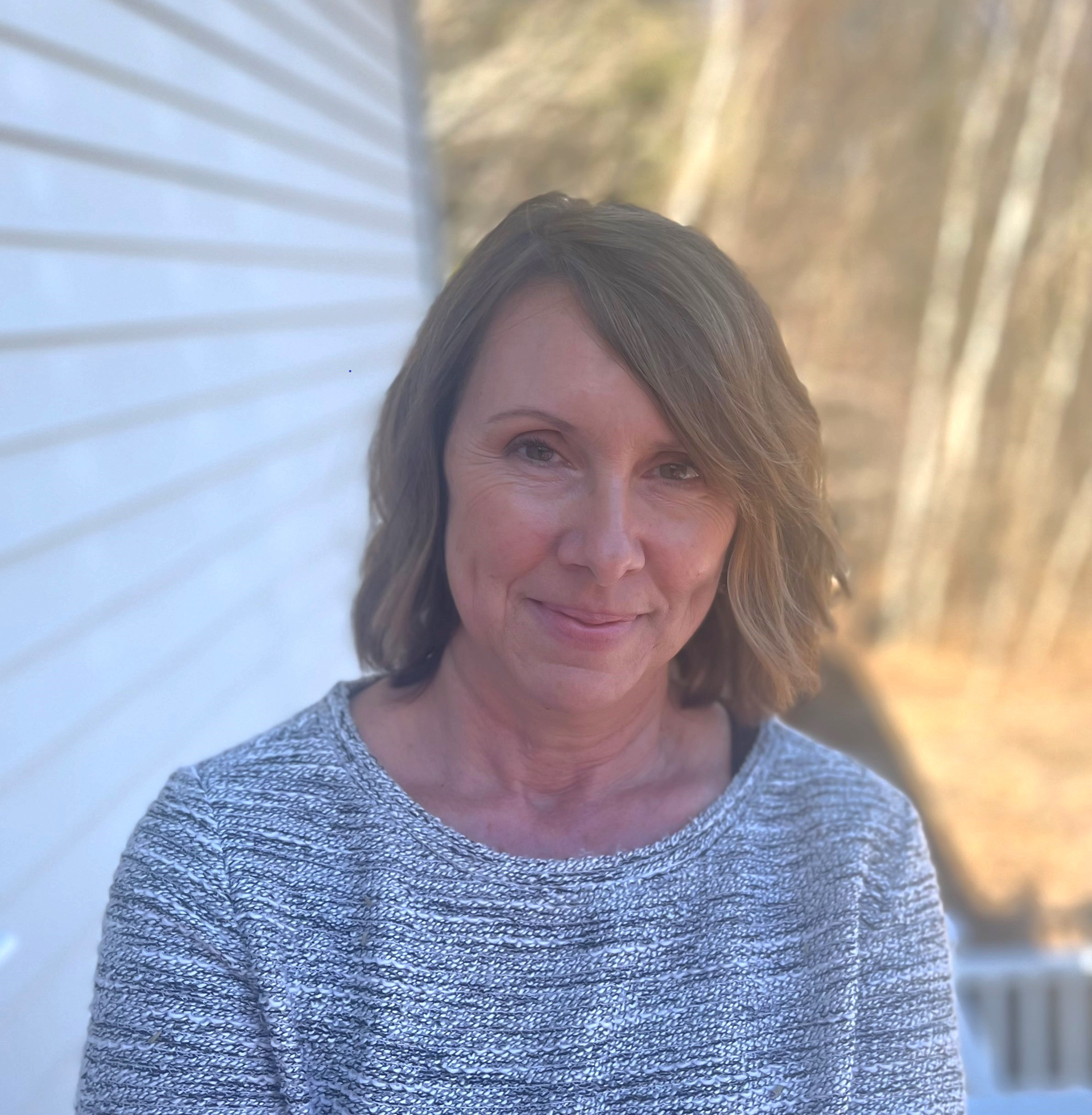 A woman in a grey sweater is smiling for the camera.