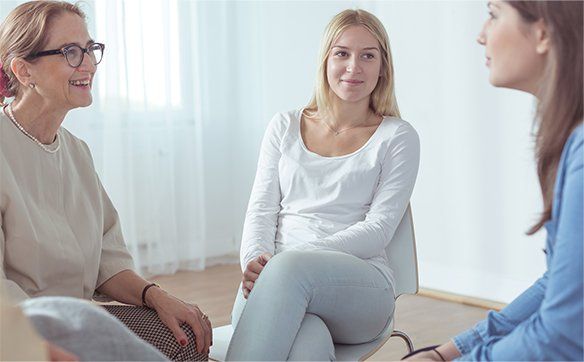 Three women are sitting in chairs talking to each other.