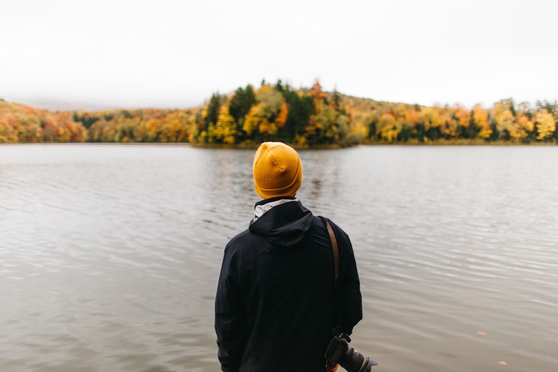 A man in a yellow hat is standing in front of a lake