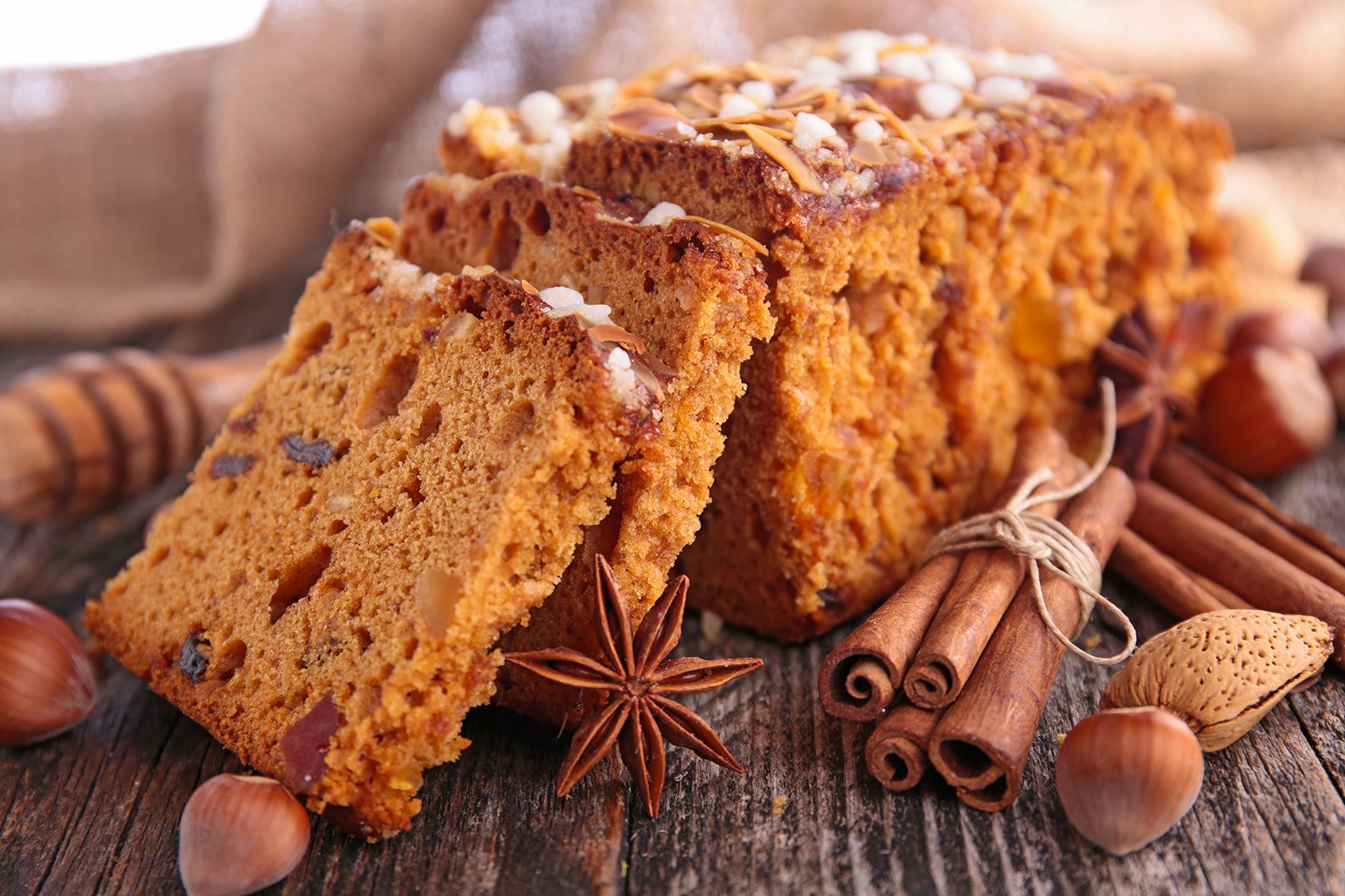 Er ligt een kruidkoek met wat plakjes op een tafel met kaneel, ster anijs en noten daar omheen