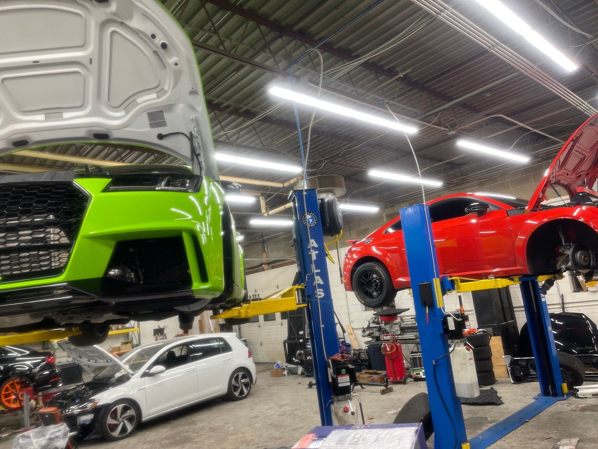 Cars being worked on in a garage. Green, red, and white vehicles are on lifts. | A2B Euro Car Repair
