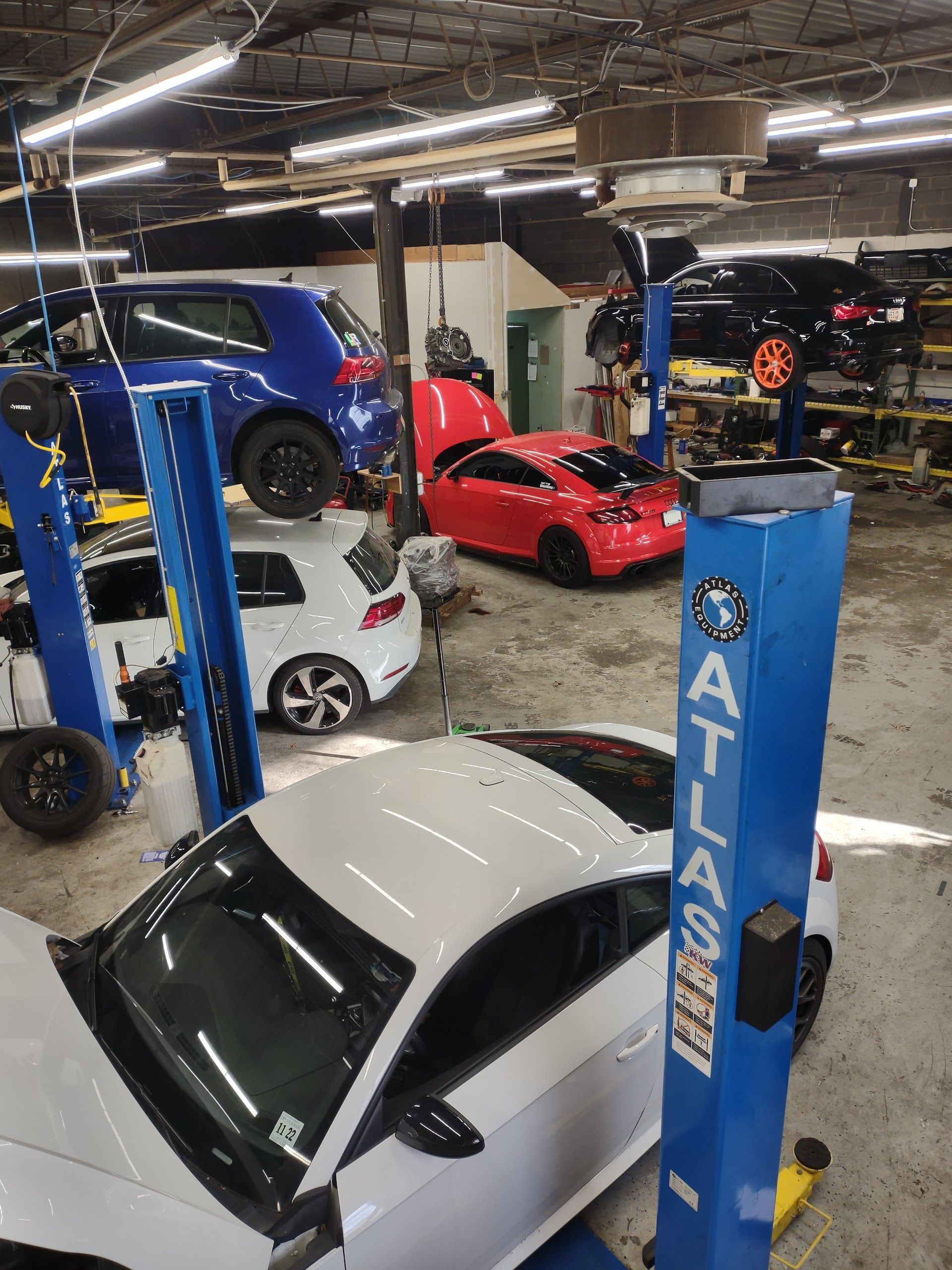 Cars on lifts in a busy auto repair shop, including a white, red, and blue vehicles. | A2B Euro Car Repair