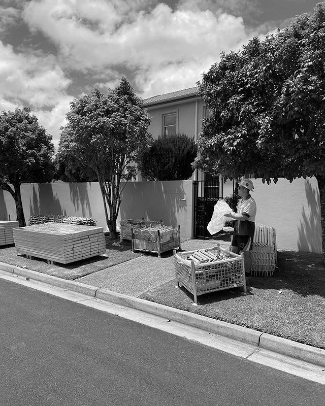 A Black and White Photo of a Man Sitting at a Table in Front of a House — RM Scaffolding Solutions in Byron Bay, NSW
