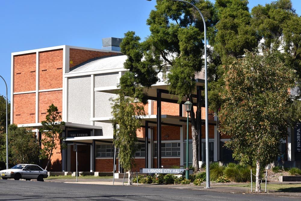 A White Car is Driving Past a Large Brick Building — RM Scaffolding Solutions in Lismore, NSW