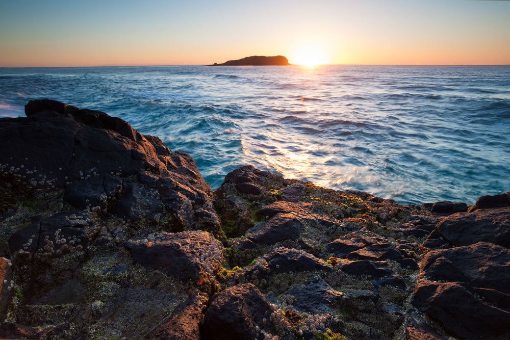 The Sun is Setting Over the Ocean With a Small Island in the Distance — RM Scaffolding Solutions in Tweed Coast, NSW