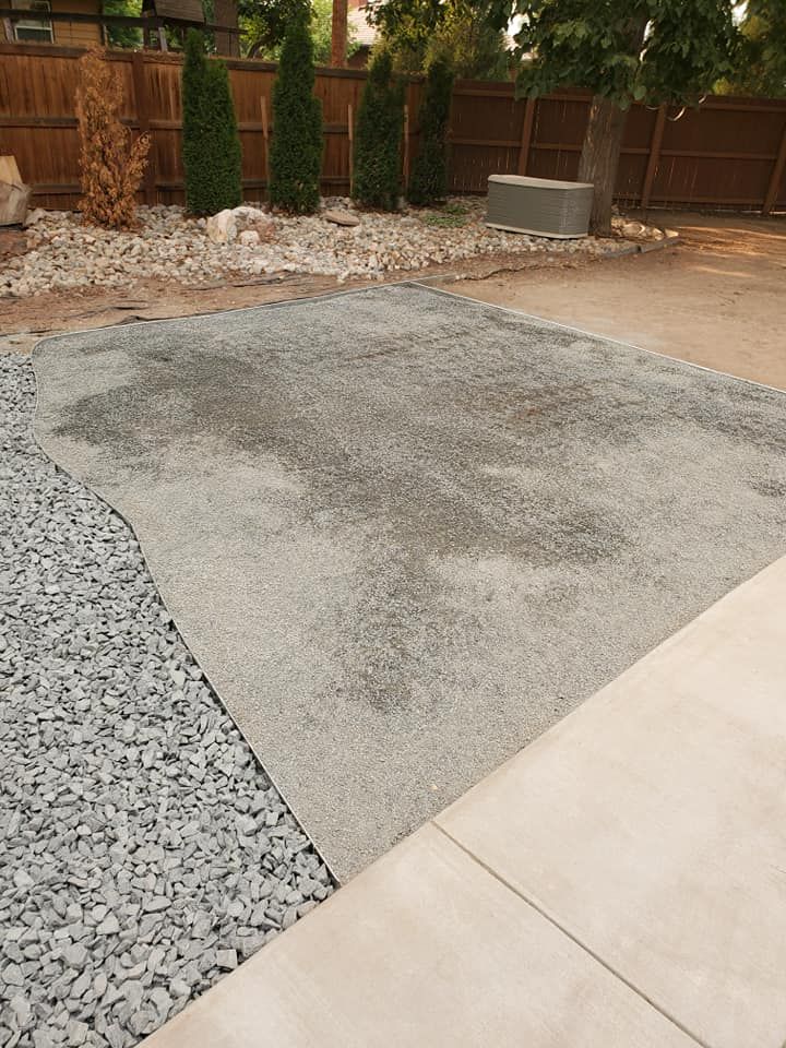 A gravel patio under construction next to a concrete patio, with landscaping in the background.