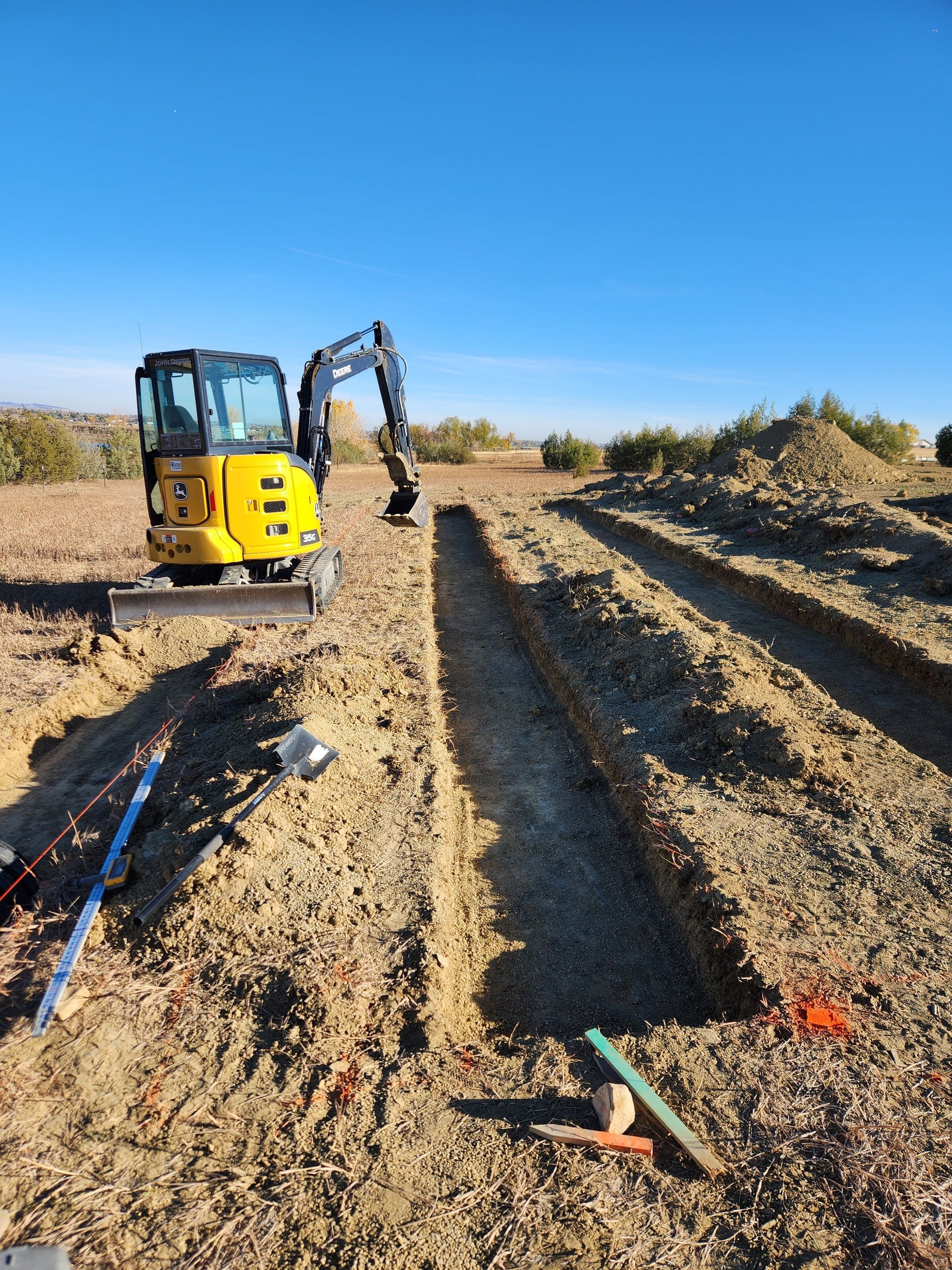 A yellow excavator digging a trench in a field under a clear blue sky.