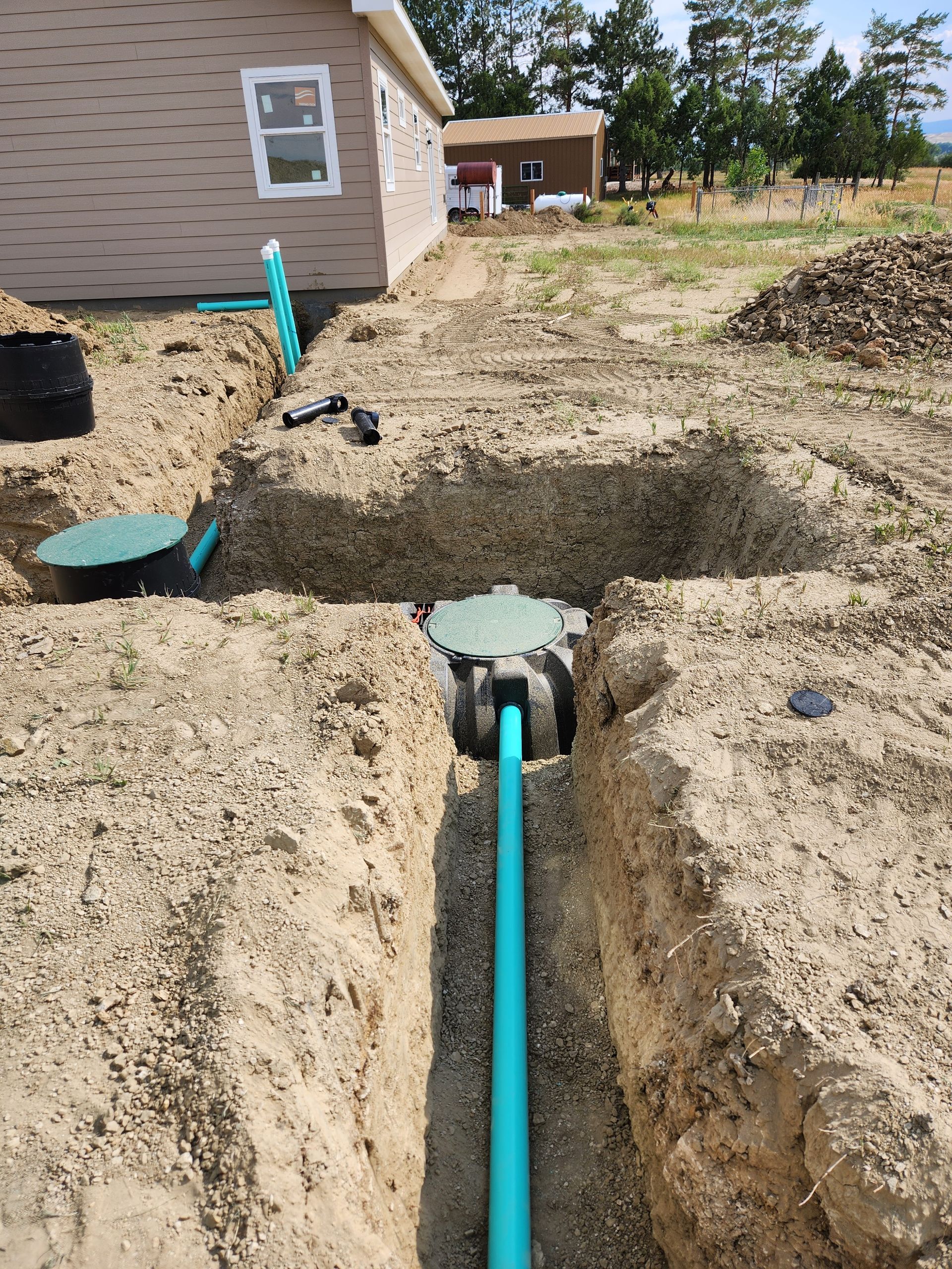 Installation of a septic system: trench with blue pipe, access lids, connecting to a building.